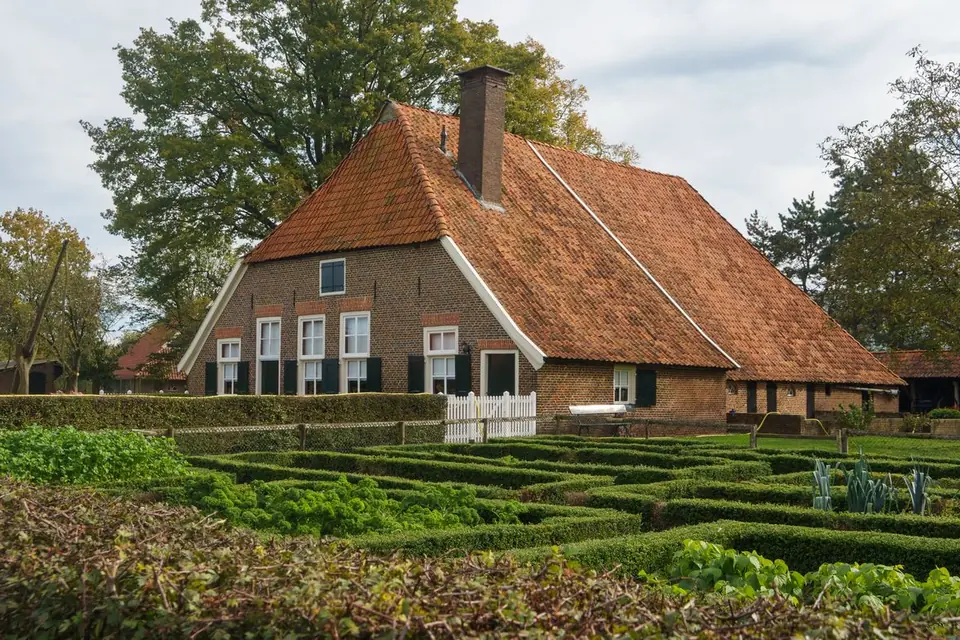 Oude boerderij met pannendak achter een moestuin met hagen