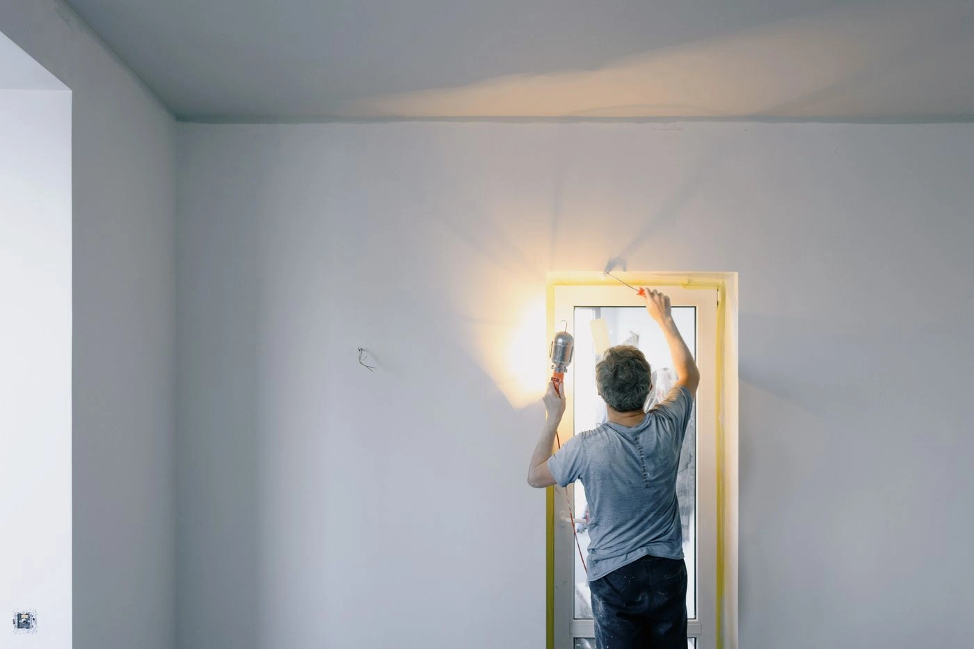 Vakman schildert een deurkozijn in een lichte kamer, bij het licht van een werklamp
