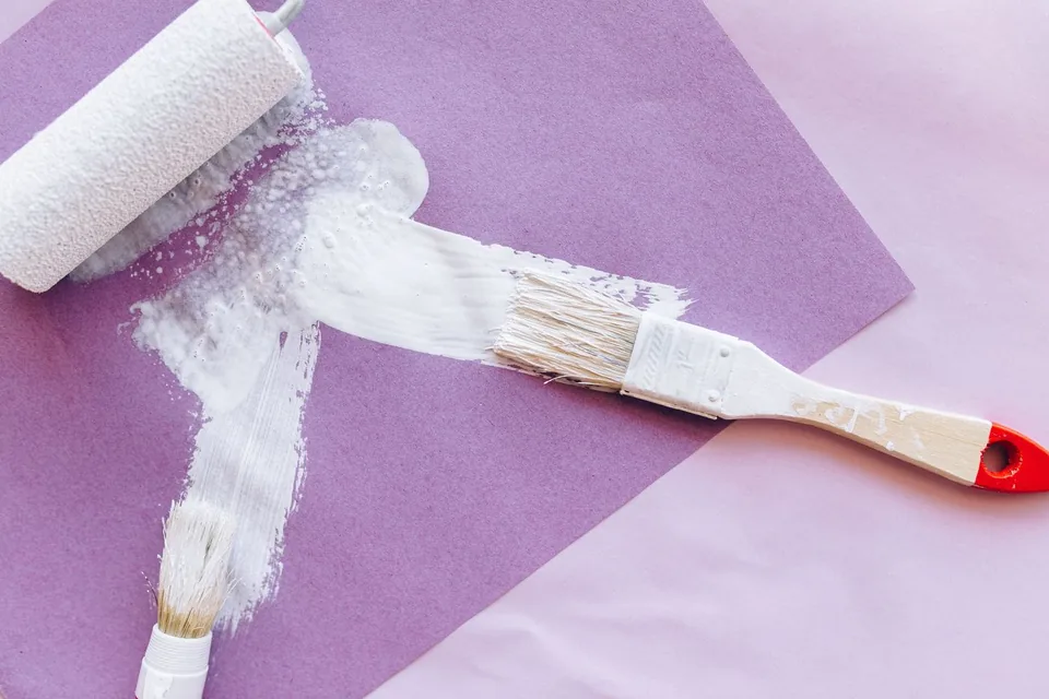 Verfroller en kwast met witte verf op een vel papier