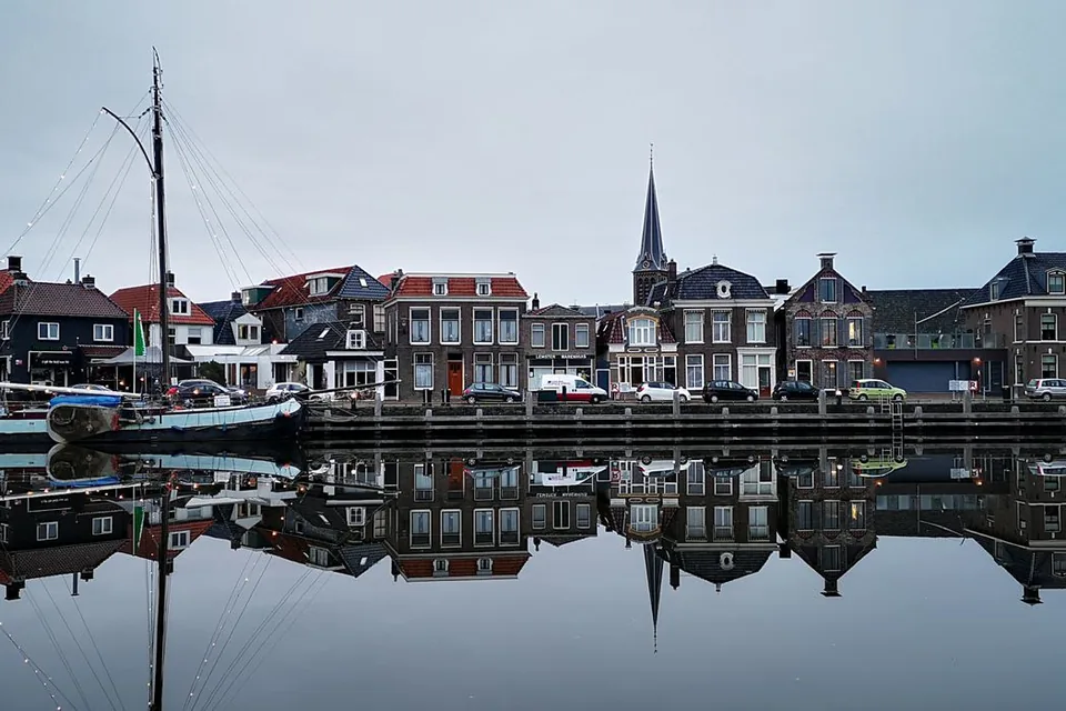 Rij oude huizen en een kerktoren weerspiegeld in het water van een klein Hollands stadje